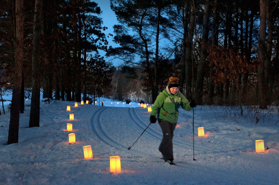 A woman cross-country skiing in winter at night in Wisconsin, glowing lanterns lighting the path