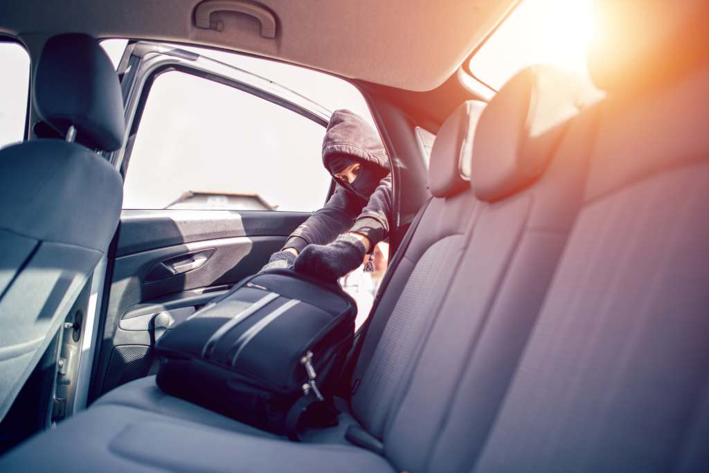 Road Trip Tips: Protecting Your Belongings While Traveling for Assignments A thief in a mask stealing a backpack from a car. The accompanying webpage article provides tips for healthcare travelers to protect their belongings during assignments. One of the key recommendations is to park in a well-lit area.
