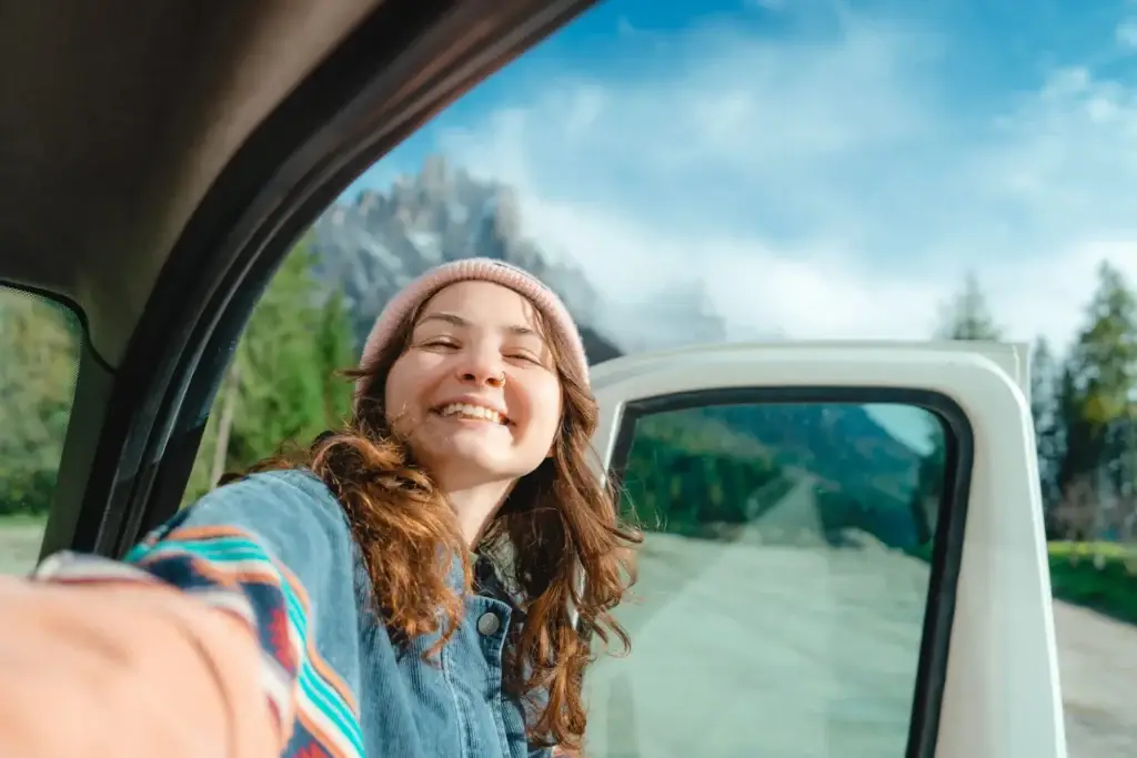 A woman smiling and taking a selfie in a car, with a mountainous landscape visible through the window. The article provides various tips for healthcare travelers to protect their belongings during road trips for assignments