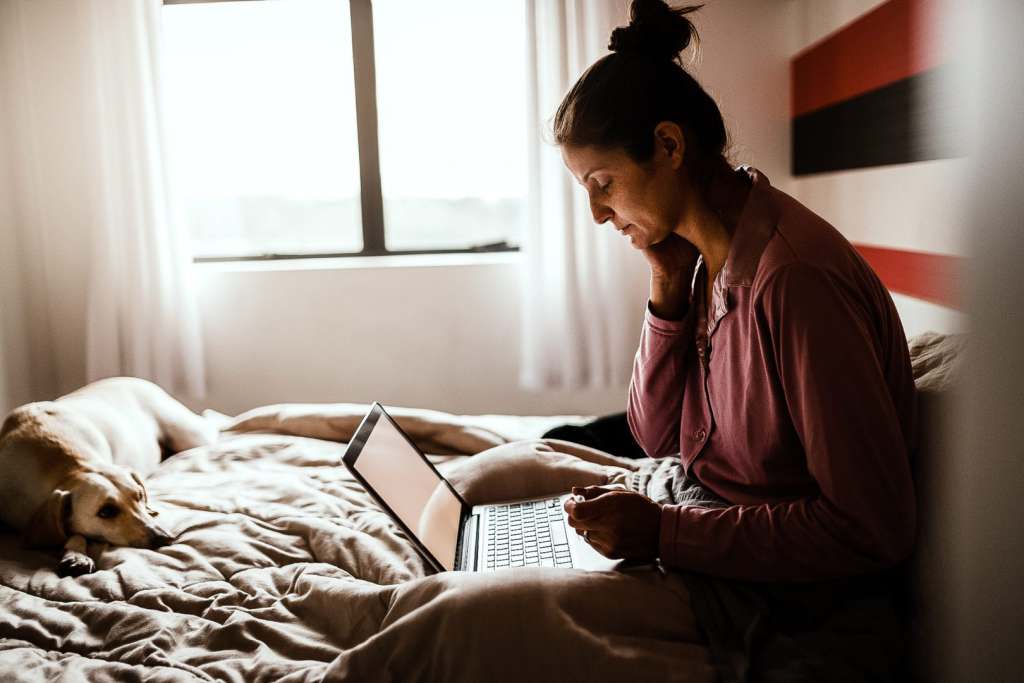 What To Do If You’ve Been Exposed to COVID-19 Sick woman making an appointment with doctor via internet with her dog on bed