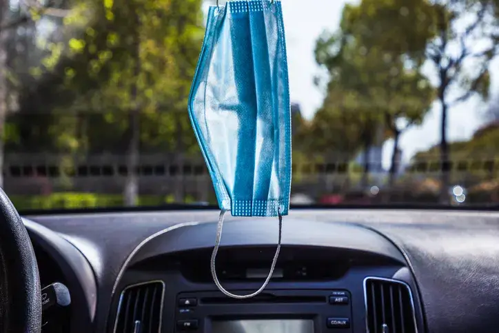 A disposable medical mask is hung on the front of the car