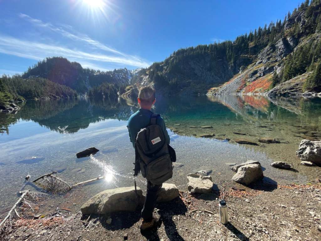 Helpful Travel Nursing Tips for a Good Work-Life Balance Male hiker with backpack looks out at lake and mountain landscape