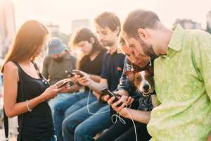 Group of people playing games on their cell phones. Group of young people on their cell phones with a dog.