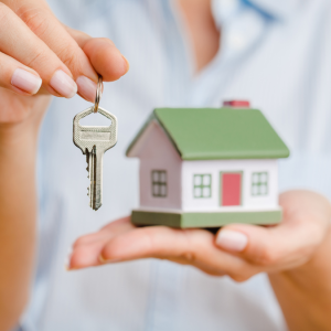 Hands holding miniature house and a house key.