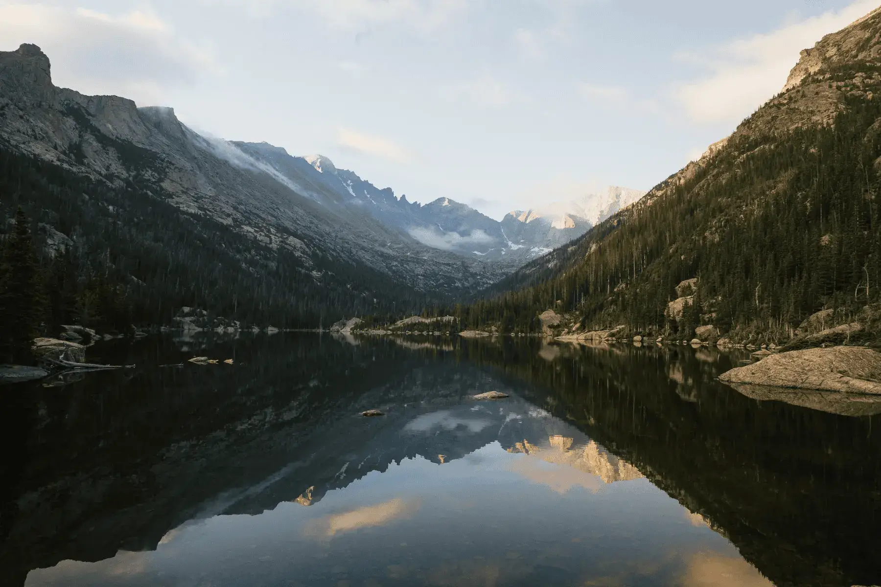 5 Mountainous National Parks and Top Hikes for the Best Views A picture of a mountain lake view surrounded by trees in the early morning