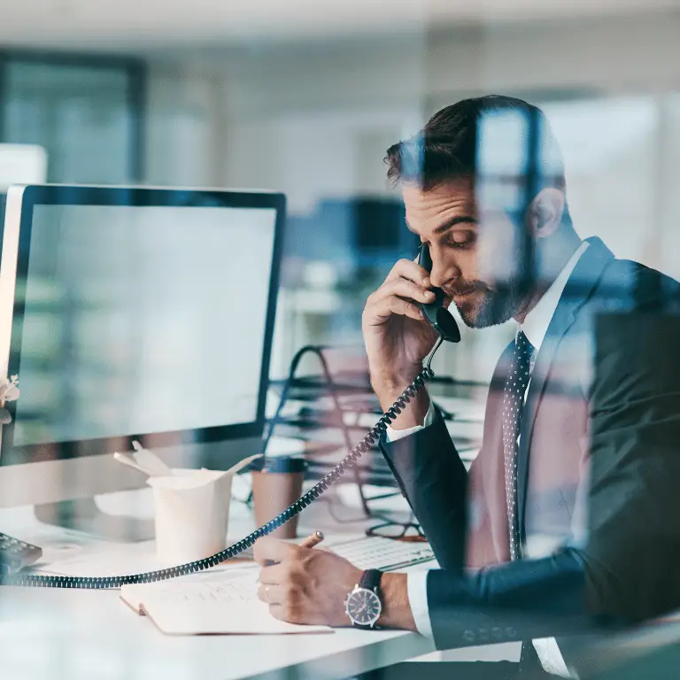 Non-clinical healthcare professional speaking on the phone while working at a computer in an office.