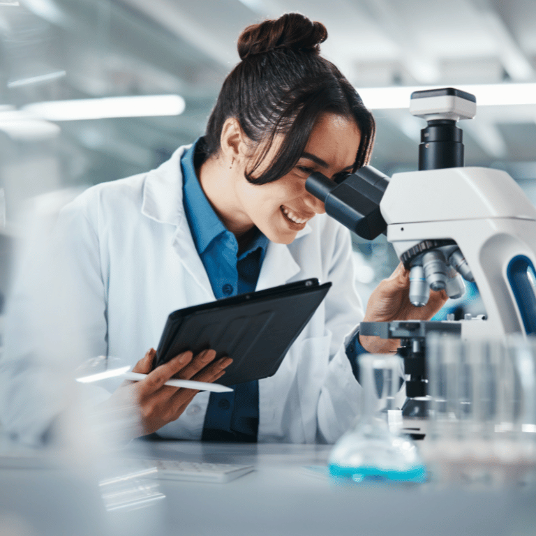 Life sciences professional in a laboratory using a microscope while holding a tablet.