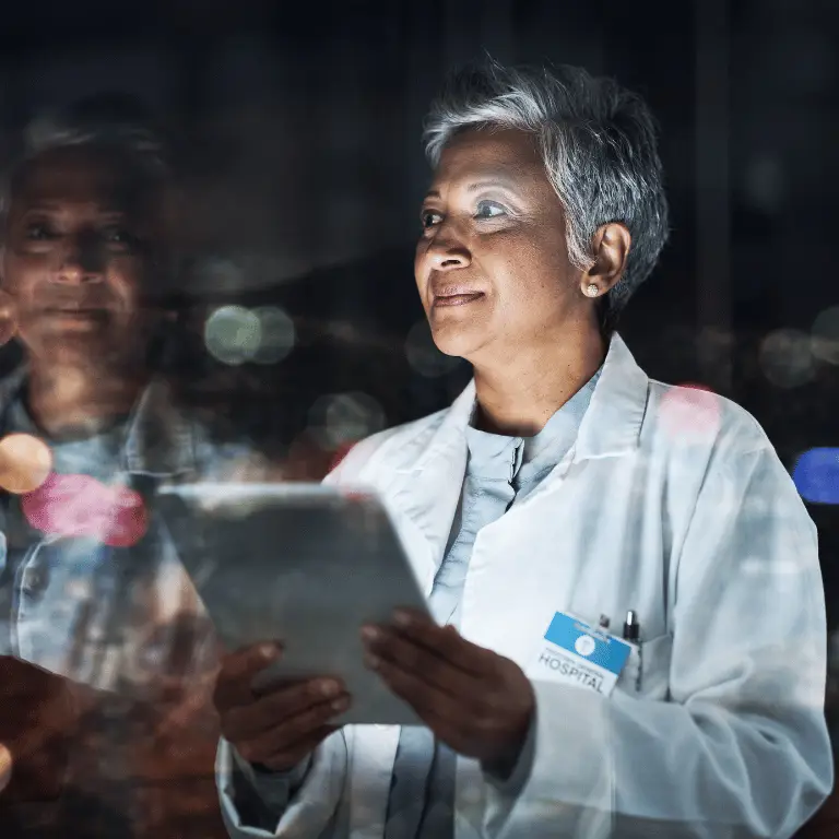 Healthcare provider in a white coat holding a tablet in a hospital setting.