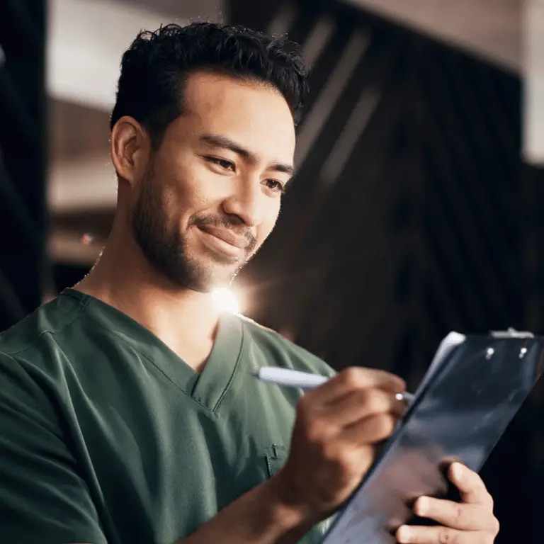 Healthcare professional in green scrubs reviewing and writing on a clipboard.