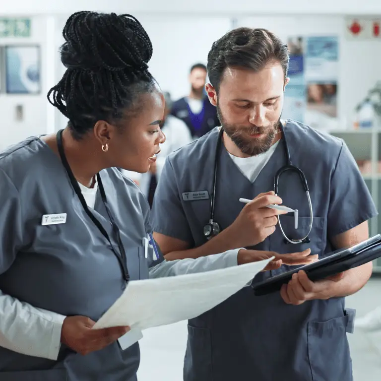 Two healthcare professionals in scrubs reviewing patient information together in a hospital setting.