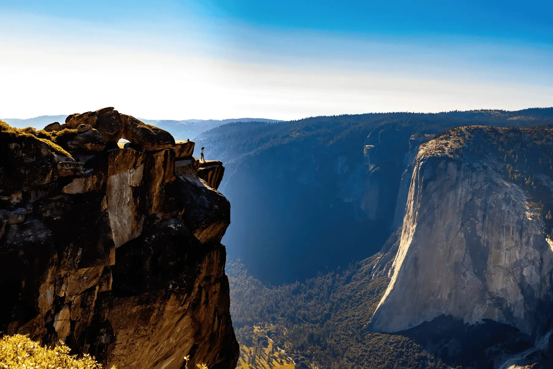 5 Mountainous National Parks and Top Hikes for the Best Views view of a woman standing on edge of mountain overlooking mountain valley