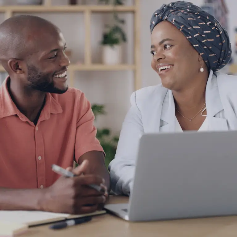 Two health plan professionals smiling and collaborating at a laptop in an office setting.
