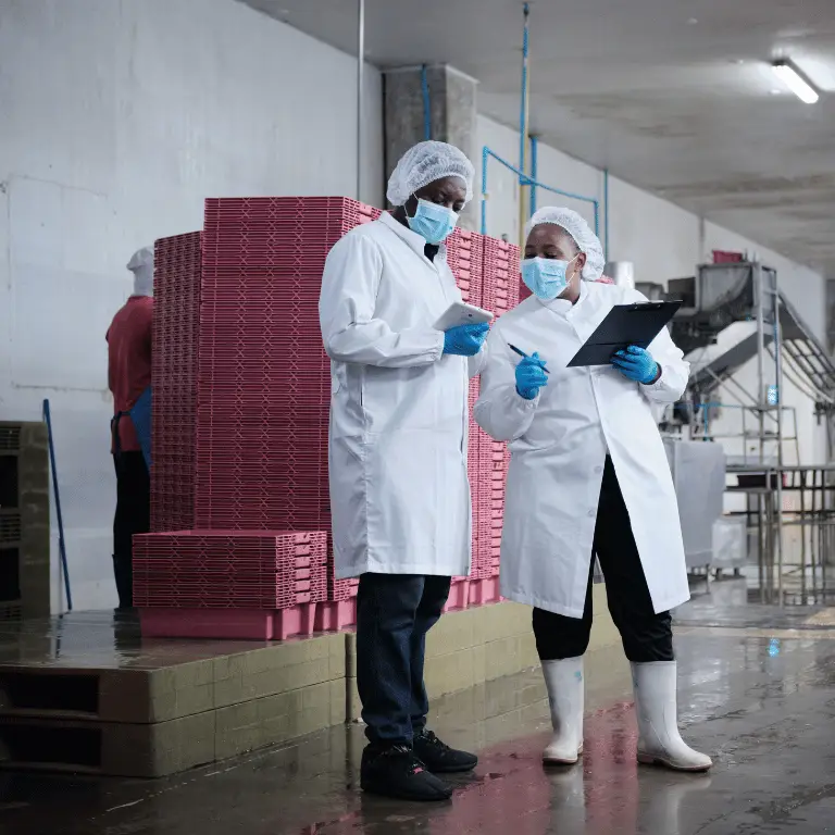 Two quality professionals in protective clothing reviewing documentation in a manufacturing facility.